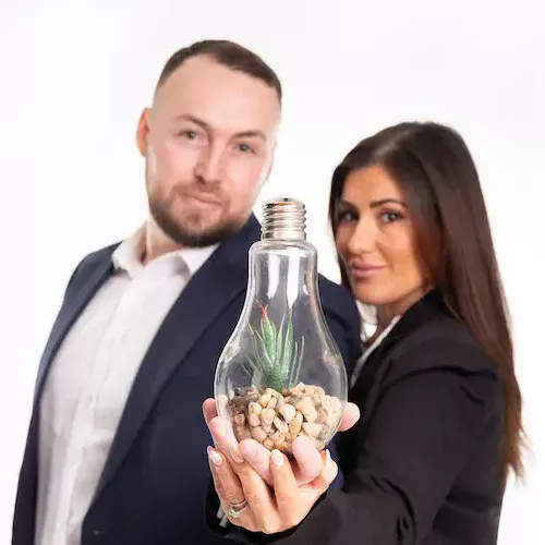 Two business professionals holding a lightbulb filled with small stones and a green plant, symbolising innovation and business growth.