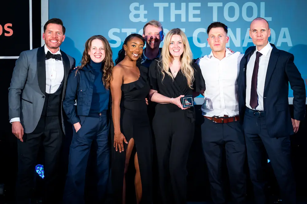 Group of formally dressed people posing on stage with an award trophy in front of a screen displaying "& The Tool Store Canada"