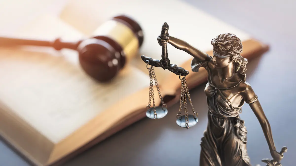 Bronze Lady Justice statue holding scales beside a wooden gavel resting on an open law book