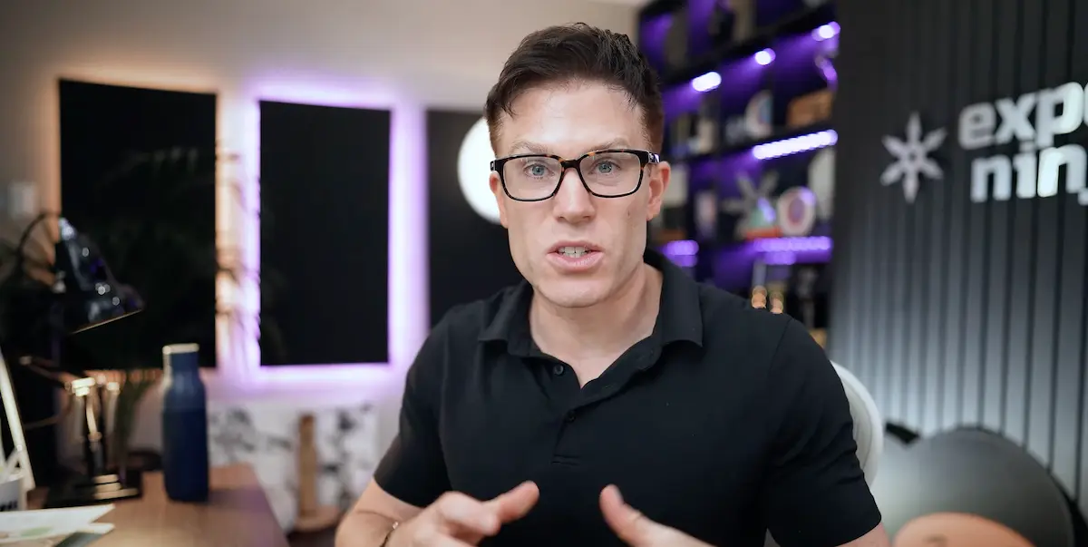 Man in glasses and a black polo shirt speaking to camera in an office with purple LED lighting and the Exposure Ninja logo visible on the wall